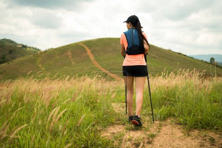 Photo for Young women active trail running across a meadow on a grassy trail high in the mountains in the afternoon with trekking pole - Royalty Free Image