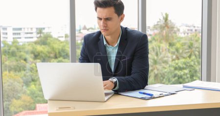 Téléchargez les photos : Homme d'affaires utilisant un ordinateur portable et contemplant tout en travaillant à son bureau dans le bureau. - en image libre de droit