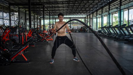 Photo for Man doing battle ropes exercise in a fitness gym. Shirtless fitness young sports man training .work out healthy. exhausted, tired out. struggle .difficult - Royalty Free Image