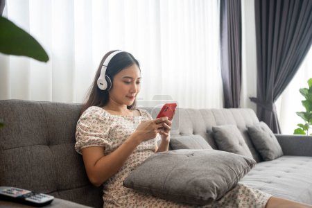 Foto de Mujer con auriculares y escuchando música y cantando feliz en casa de vacaciones y feliz en el sofá de la sala de estar - Imagen libre de derechos