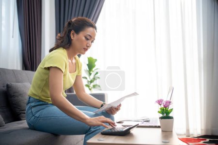 Mujer que usa la calculadora para verificar la suma total de las facturas del hogar