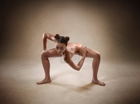 Schöne nackte sexy Fitness-Mädchen mit großer Figur beugt ihren perfekten Körper in einer Yoga-Pose im Studio. Spinnenpose.