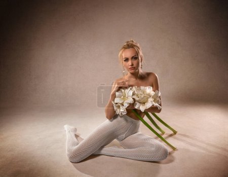 Schöne Fitness-Frau mit perfekten Beinen in weißen Netzstrumpfhosen und mit Amaryllis-Blumen - Modestil auf dem Studiohintergrund.