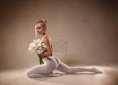 Beautiful fitness woman with perfect legs and butt in white fishnet pantyhose and with Amaryllis flowers - fashion style on the studio background.