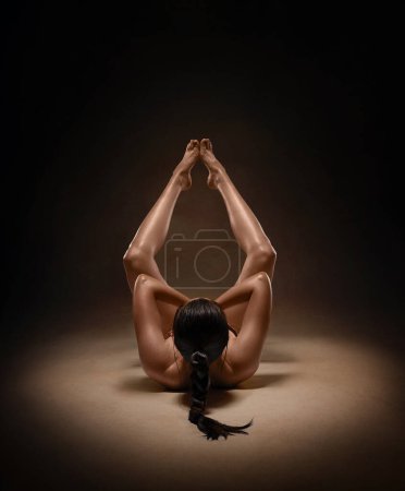 Beautiful nude sexy fitness girl with great figure flexing her perfect body in a yoga pose at the studio.