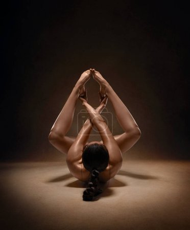 Beautiful nude sexy fitness girl with great figure flexing her perfect body in a yoga pose at the studio. Spider pose.