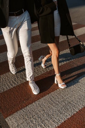 Téléchargez les photos : Jeune couple de mode traversant la rue. Gros plan jambes homme et femme sur le passage supérieur - en image libre de droit