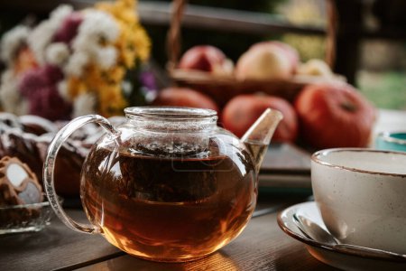 Photo for Autumn tea concept. Black tea in a glass teapot on wooden table with fall decor - Royalty Free Image