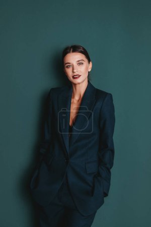 Photo for Fashionable confident woman wearing elegant green suit with blazer and trousers posing on green wall background. Studio fashion portrait - Royalty Free Image