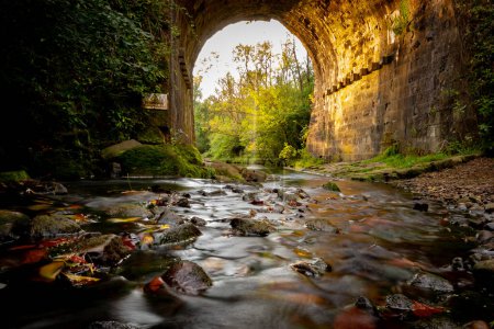 Photo for Stream with an autumn leaves and pebbles under a viaduct in Daisy Nook park Oldham England - Royalty Free Image