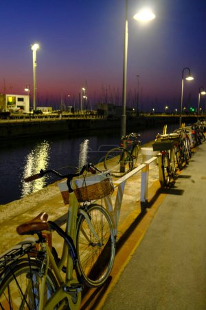 Foto de Bicicletas estacionadas en el puerto de Senigallia, Italia por la noche. Luces, farolas y reflejos de agua en la ciudad - Imagen libre de derechos