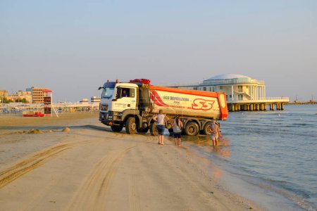 Foto de Julio 2022 Senigallia, Italia: Maquinaria pesada limpiando arena en la playa a través del horizonte del amanecer - Imagen libre de derechos