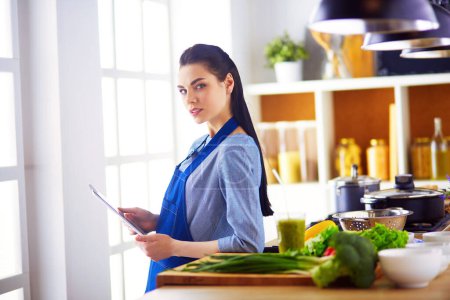 Photo for Young woman using a tablet computer to cook in her kitchen. - Royalty Free Image