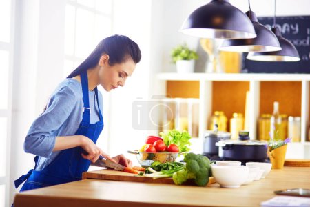 Téléchargez les photos : Jeune femme coupant des légumes dans la cuisine à la maison. - en image libre de droit