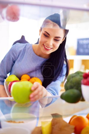 Téléchargez les photos : Femme souriante sortant un fruit frais du réfrigérateur, concept d'aliments sains. - en image libre de droit