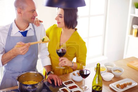 Photo for Attractive couple in love cooking and opens the wine in the kitchen while they cook dinner for a romantic evening. - Royalty Free Image