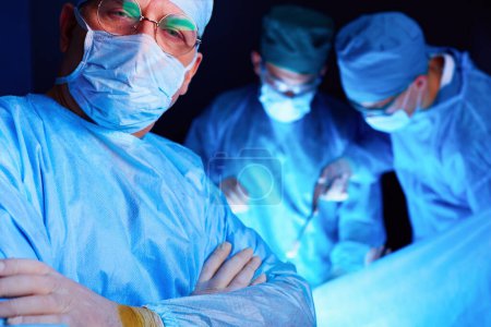 Photo for Group of surgeons at work in operating theater toned in blue. Medical team performing operation. - Royalty Free Image