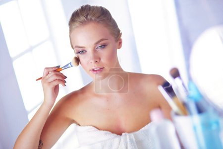 Téléchargez les photos : Une photo d'une jeune femme appliquant de la poudre visage dans la salle de bain. - en image libre de droit