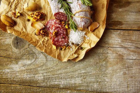 Foto de Salami italiano con sal marina, romero, ajo y nueces sobre papel. Estilo rústico. Vista superior. - Imagen libre de derechos