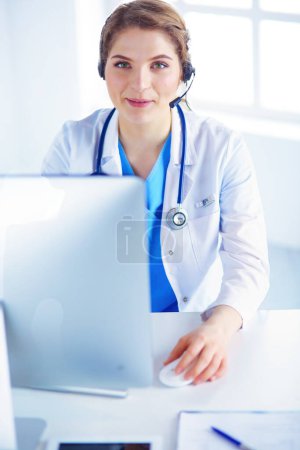 Téléchargez les photos : Médecin portant un casque assis derrière un bureau avec ordinateur portable. - en image libre de droit