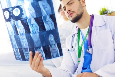 Téléchargez les photos : Médecin attrayant examinant une radiographie et souriant à la caméra - en image libre de droit