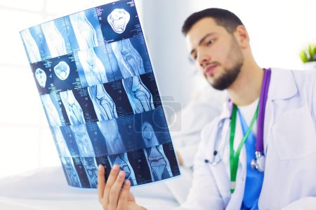 Foto de Atractivo médico examinando una radiografía y sonriendo a la cámara - Imagen libre de derechos