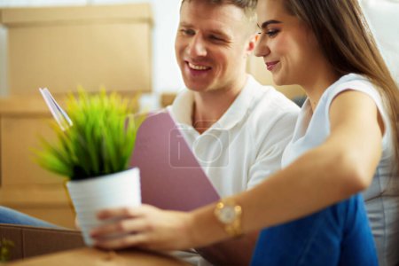 Photo for Young couple holding album while sitting on floor in new house. - Royalty Free Image