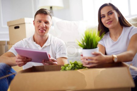 Téléchargez les photos : Couple souriant appuyé sur des boîtes dans une nouvelle maison
. - en image libre de droit