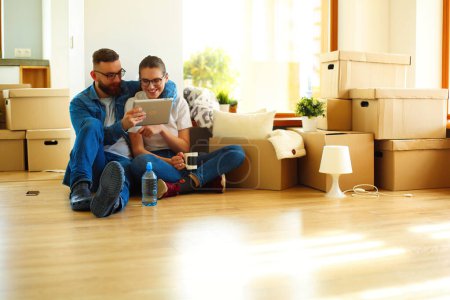 Photo for Happy young couple sitting on the floor of new house surrounded by boxes. - Royalty Free Image
