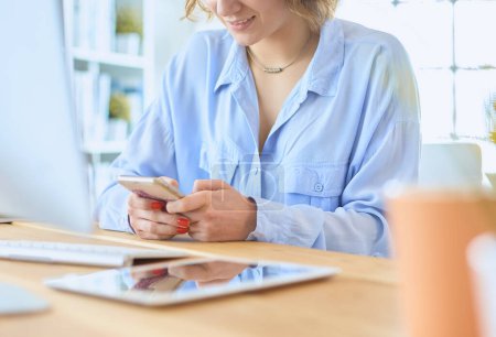 Photo for Young businesswoman text messaging while sitting at office in front of laptop. - Royalty Free Image