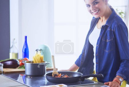 Photo for Young woman cooking healthy food holding a pan with vegetables is it. Healthy lifestyle, cooking at home concept. - Royalty Free Image