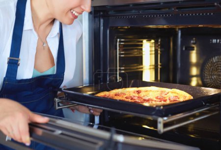 Téléchargez les photos : Joyeux jeune femme cuisine pizza à la maison. - en image libre de droit
