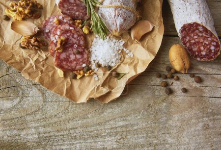 Photo for Italian salami wih sea salt, rosemary, garlic and nuts on paper. Rustic style. Top view. - Royalty Free Image