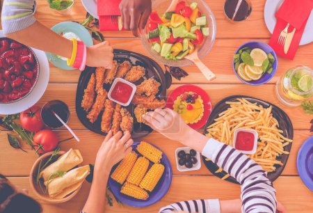 Foto de Vista superior del grupo de personas cenando juntas mientras están sentadas en la mesa de madera. Comida en la mesa. La gente come comida rápida - Imagen libre de derechos