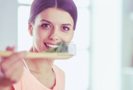 Foto de Mujer joven sonriente mezclando ensalada fresca en la cocina. - Imagen libre de derechos