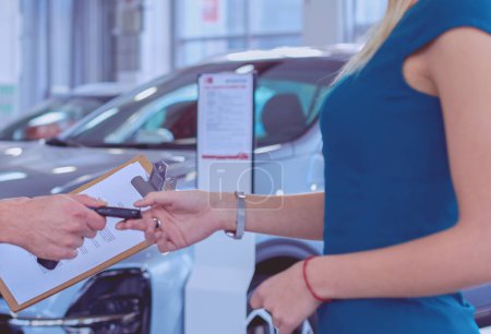 Téléchargez les photos : Vendeur de voitures vend une voiture à un client heureux dans le concessionnaire automobile et remet les clés. - en image libre de droit