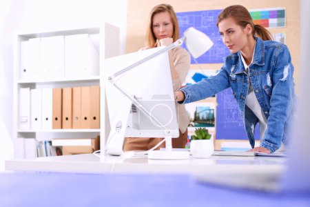 Téléchargez les photos : Deux jeunes femmes debout près du bureau avec des instruments, plan et ordinateur portable. - en image libre de droit