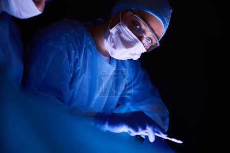 Téléchargez les photos : Équipe de médecins en chirurgie dans un fond sombre - en image libre de droit