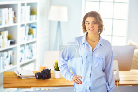 Photo for Smiling female photographer with a professional camera standing near desk. - Royalty Free Image