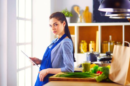 Foto de Mujer joven usando una tableta para cocinar en su cocina. - Imagen libre de derechos
