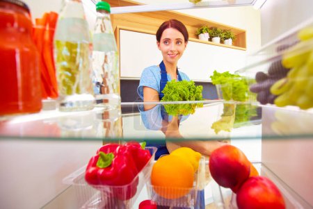 Téléchargez les photos : Portrait de femme debout près d'un réfrigérateur ouvert rempli d'aliments sains, de légumes et de fruits. Portrait de femme. - en image libre de droit