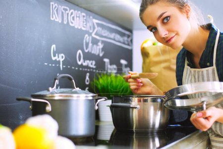 Téléchargez les photos : Jeune femme debout près de la cuisinière dans la cuisine - en image libre de droit