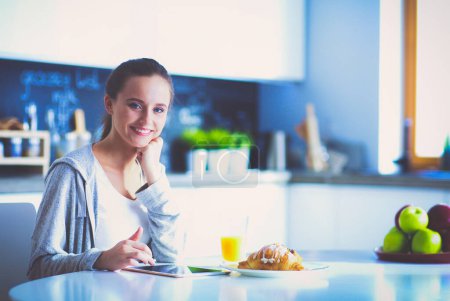 Téléchargez les photos : Jeune femme avec jus d'orange et tablette dans la cuisine - en image libre de droit