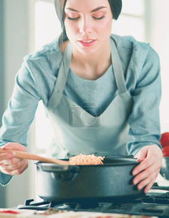 Téléchargez les photos : Femme debout près de la cuisinière dans la cuisine, cuisiner et sentir les beaux arômes - en image libre de droit