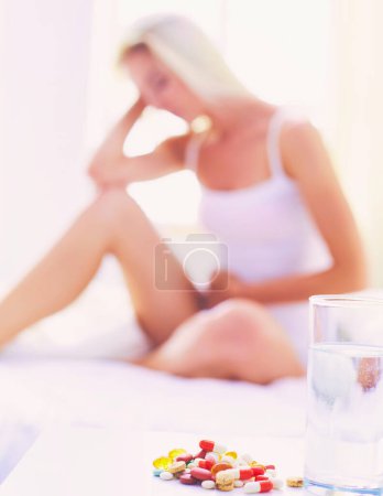 Photo for Young beautiful woman with pills sitting on bed in bedroom. - Royalty Free Image