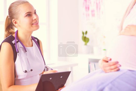Téléchargez les photos : Jeune femme médecin avec stéthoscope et tablette parlant avec une femme enceinte à l'hôpital - en image libre de droit