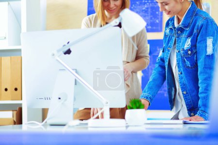 Photo for Two young woman standing near desk with instruments, plan and laptop - Royalty Free Image