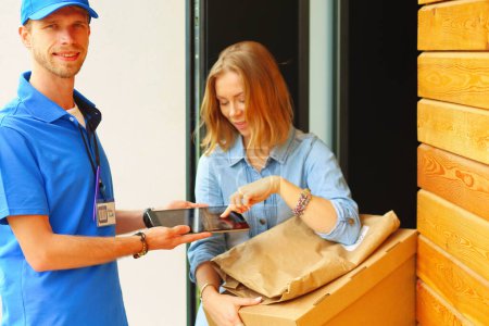 Foto de Repartidor sonriente con uniforme azul que entrega la caja de paquetes al destinatario: concepto de servicio de mensajería. Repartidor sonriente en uniforme azul. - Imagen libre de derechos