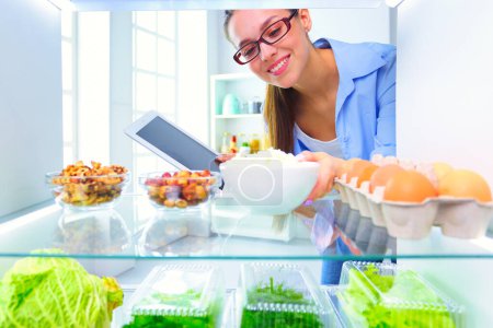 Photo for Portrait of female standing near open fridge full of healthy food, vegetables and fruits. - Royalty Free Image