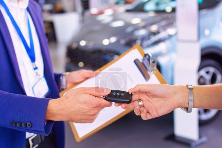 Téléchargez les photos : Vendeur de voitures vend une voiture à un client heureux dans le concessionnaire automobile et remet les clés. - en image libre de droit